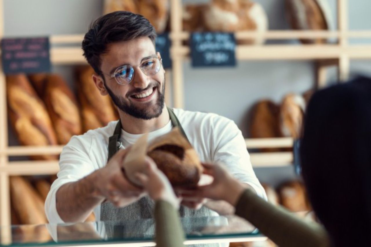 Um homem está vendendo pão para uma mulher em uma padaria.