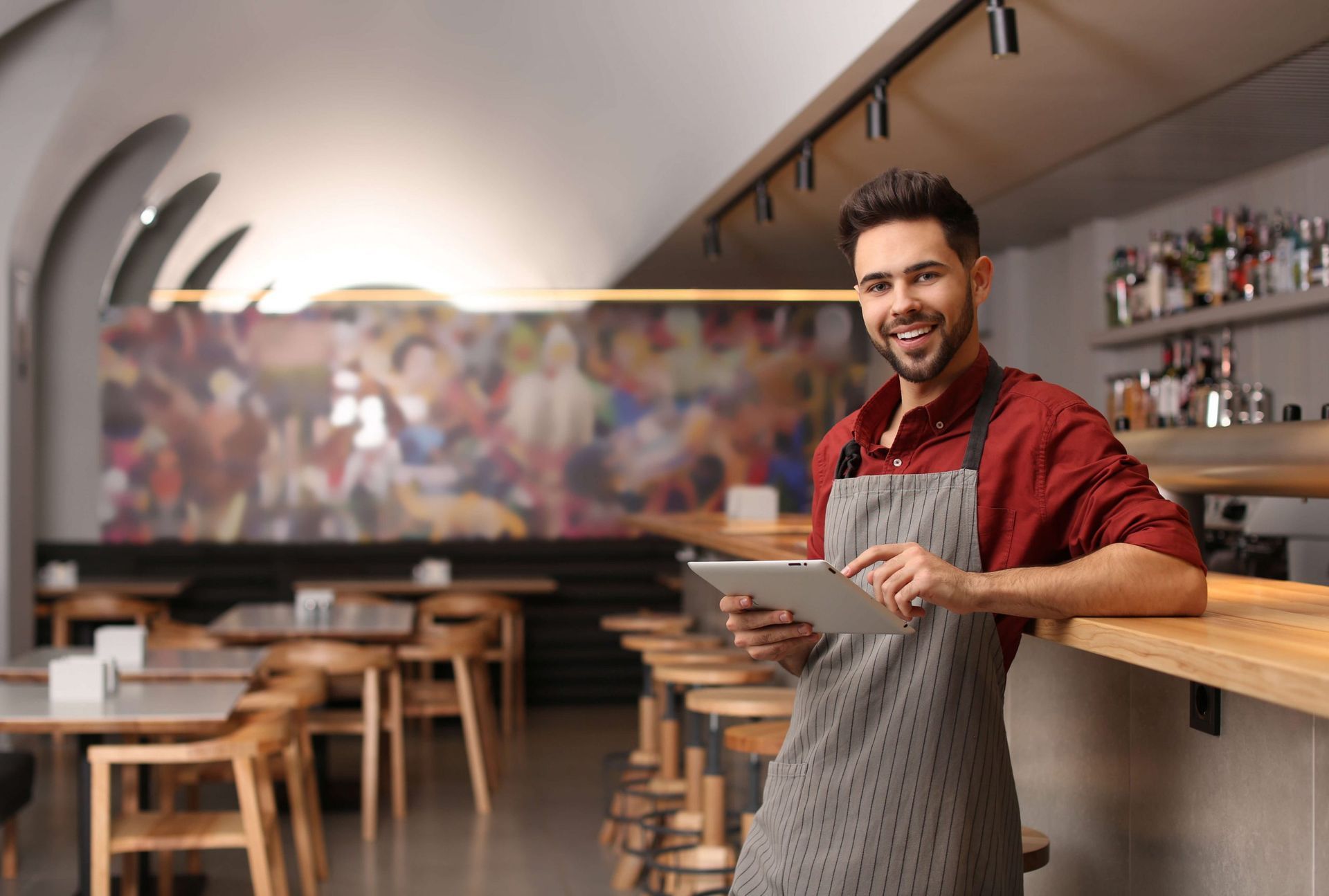 Um homem de avental está segurando um tablet em um restaurante.