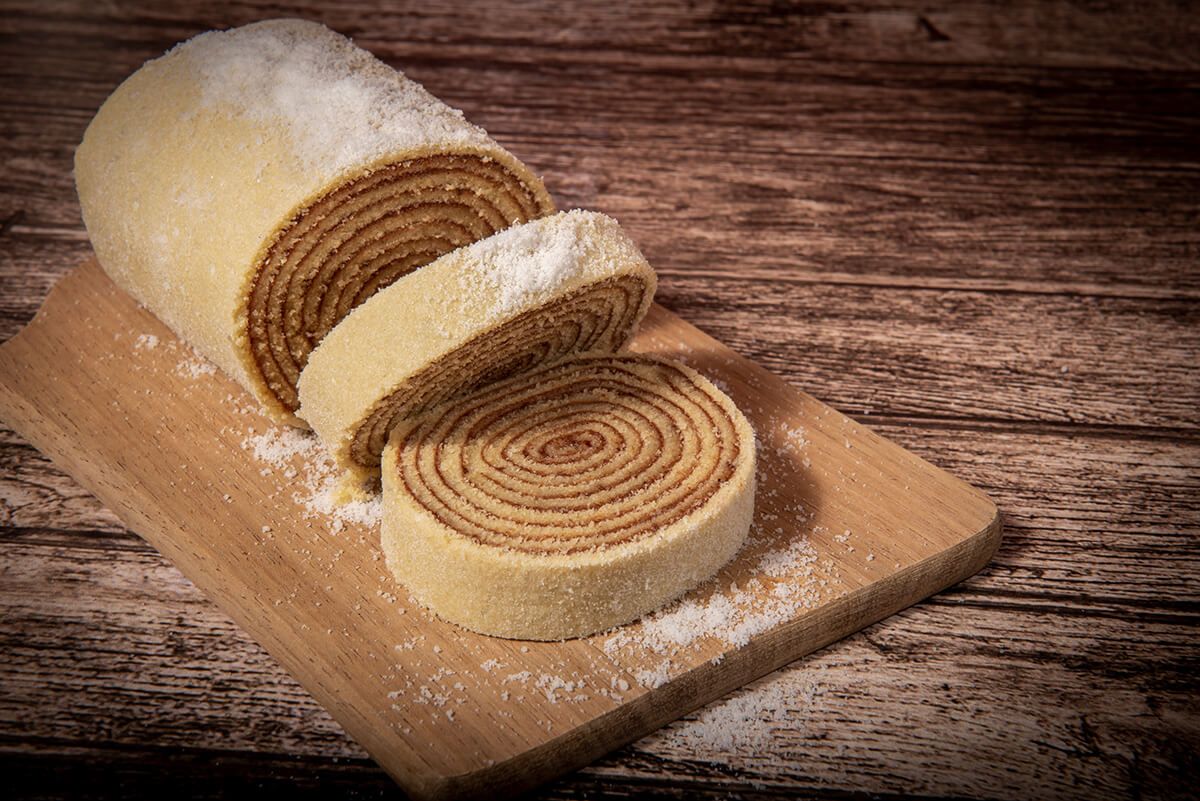 Um rolo de bolo está sobre uma tábua de corte de madeira.