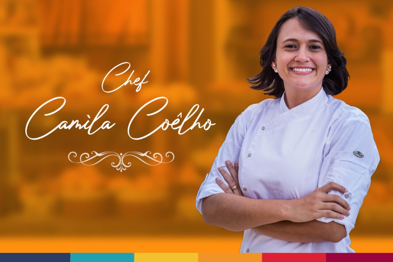 Uma mulher em uniforme de chef está sorrindo com os braços cruzados.