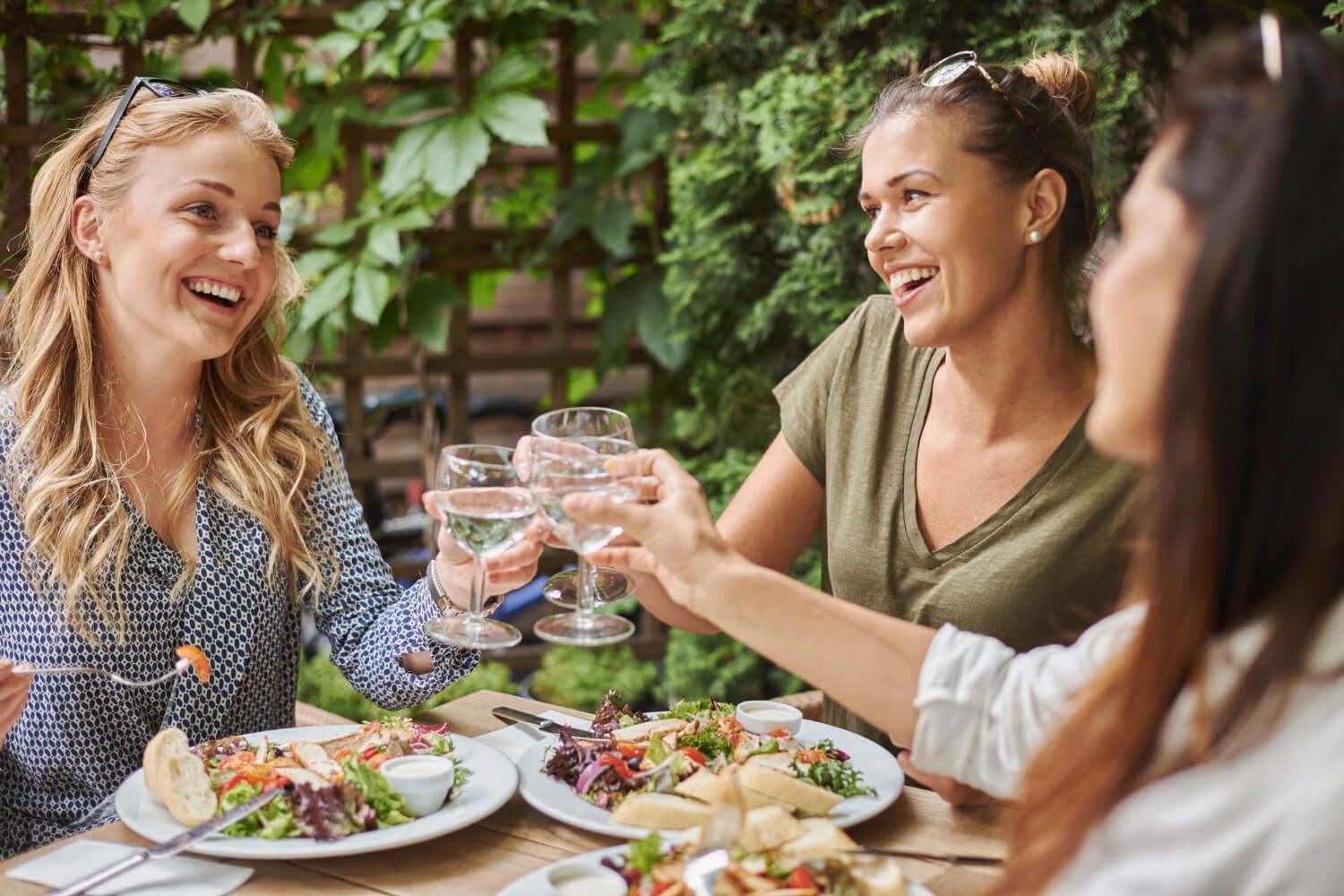 Um grupo de mulheres está sentado à mesa comendo e bebendo vinho.
