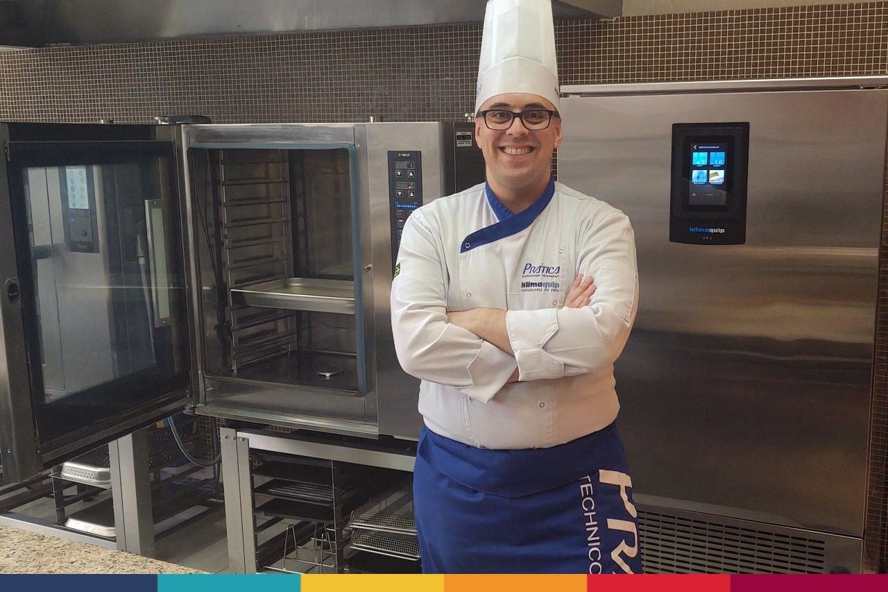 Um chef está de pé em frente a um forno com os braços cruzados.