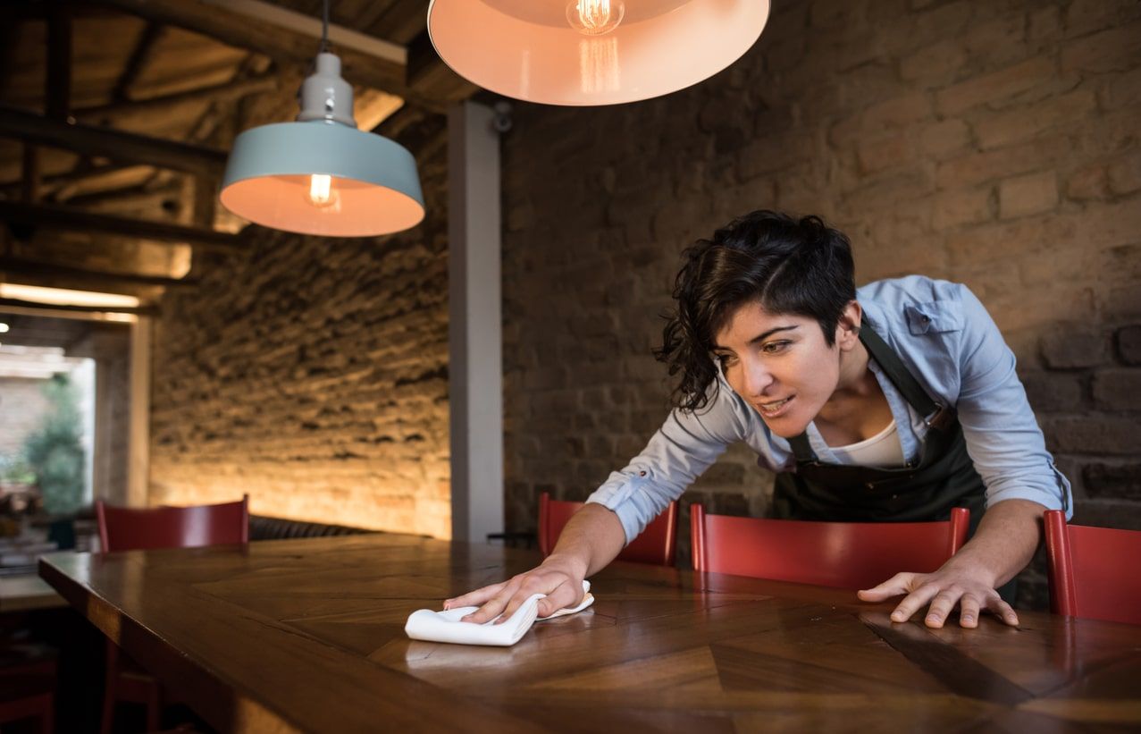 Uma mulher está limpando uma mesa de madeira em um restaurante.