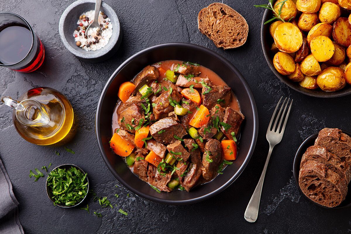 Uma tigela de ensopado de carne com cenouras e batatas sobre uma mesa.