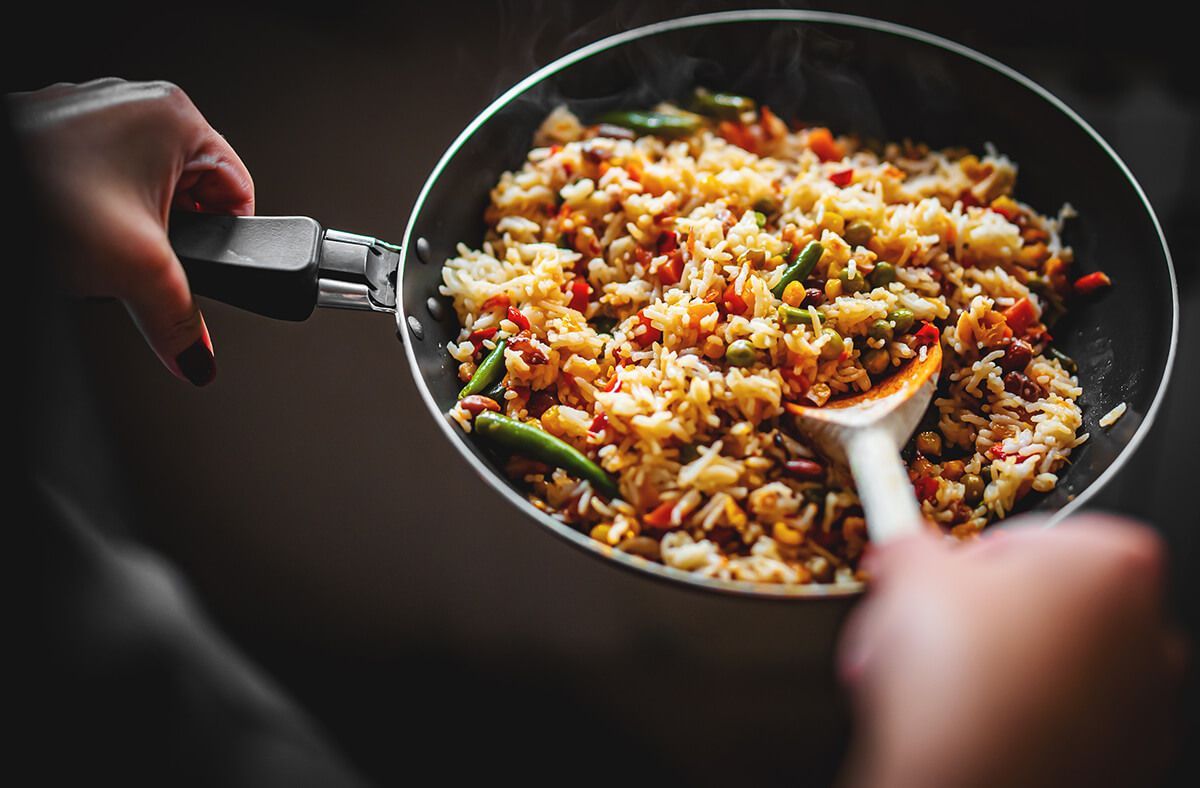 Uma pessoa está mexendo arroz em uma frigideira com uma colher de pau.