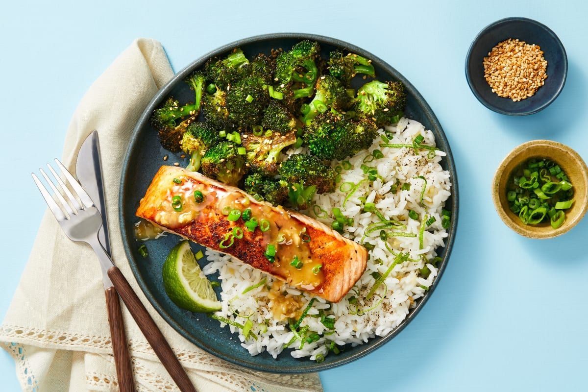 Um prato de comida com salmão, brócolis e arroz sobre uma mesa.