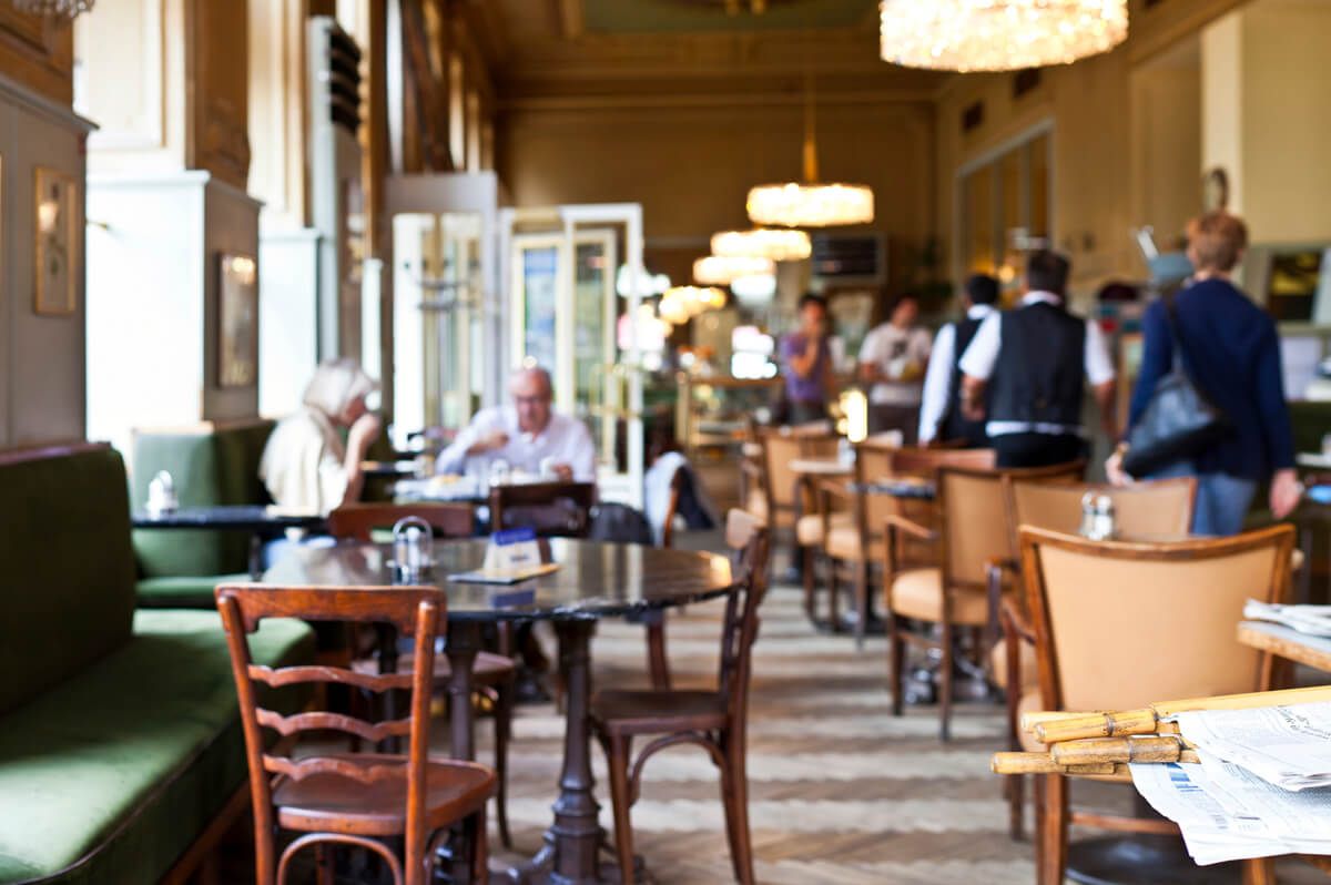 Um restaurante com mesas e cadeiras e pessoas andando por aí