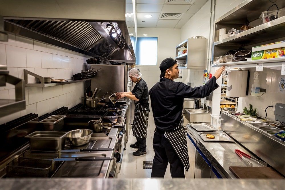 Dois chefs estão trabalhando em uma cozinha comercial preparando comida.