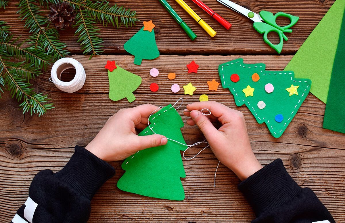 Uma criança está fazendo uma árvore de natal de feltro.