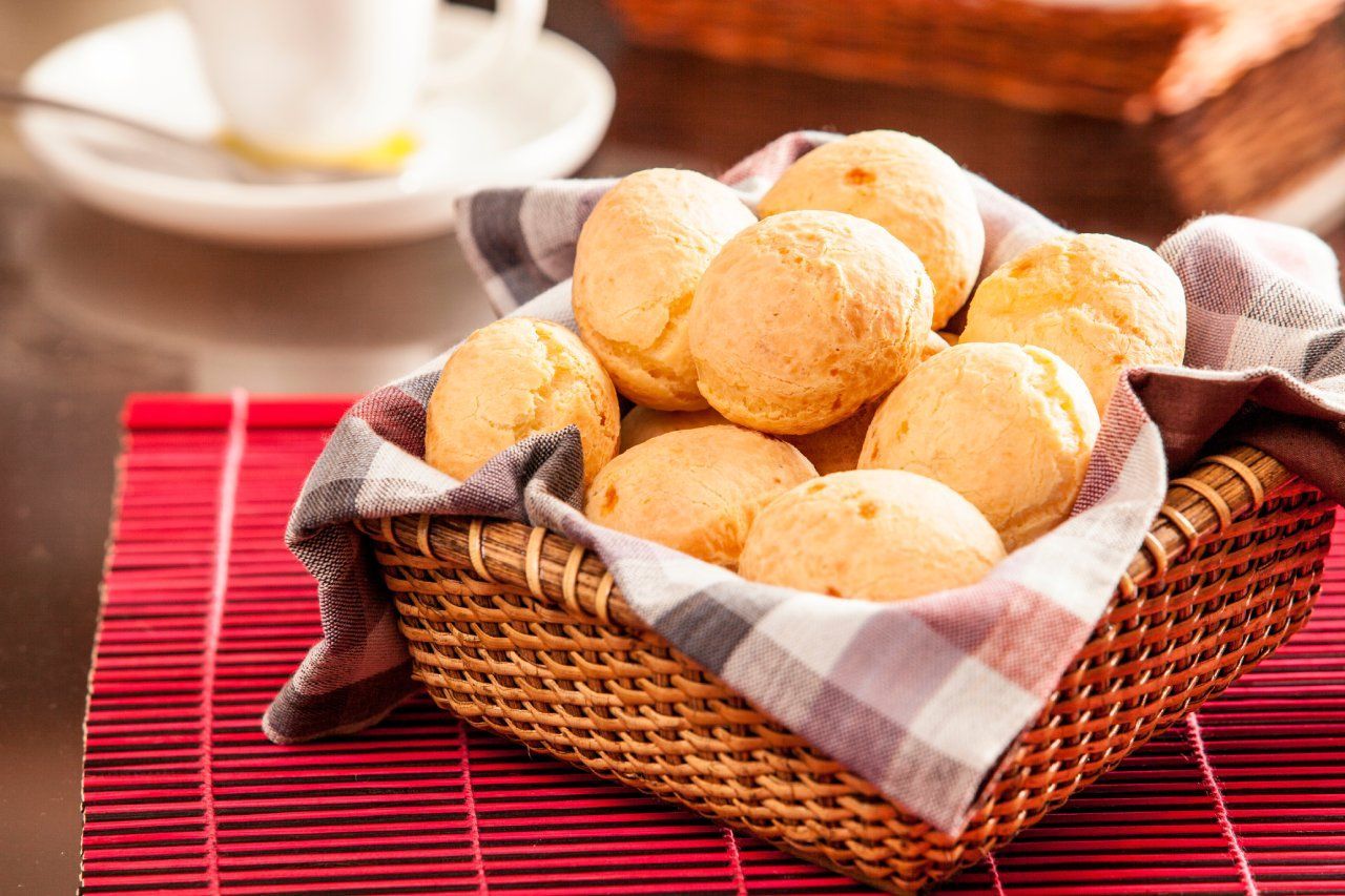 Uma cesta de bolinhas de queijo está sobre uma mesa ao lado de uma xícara de café.