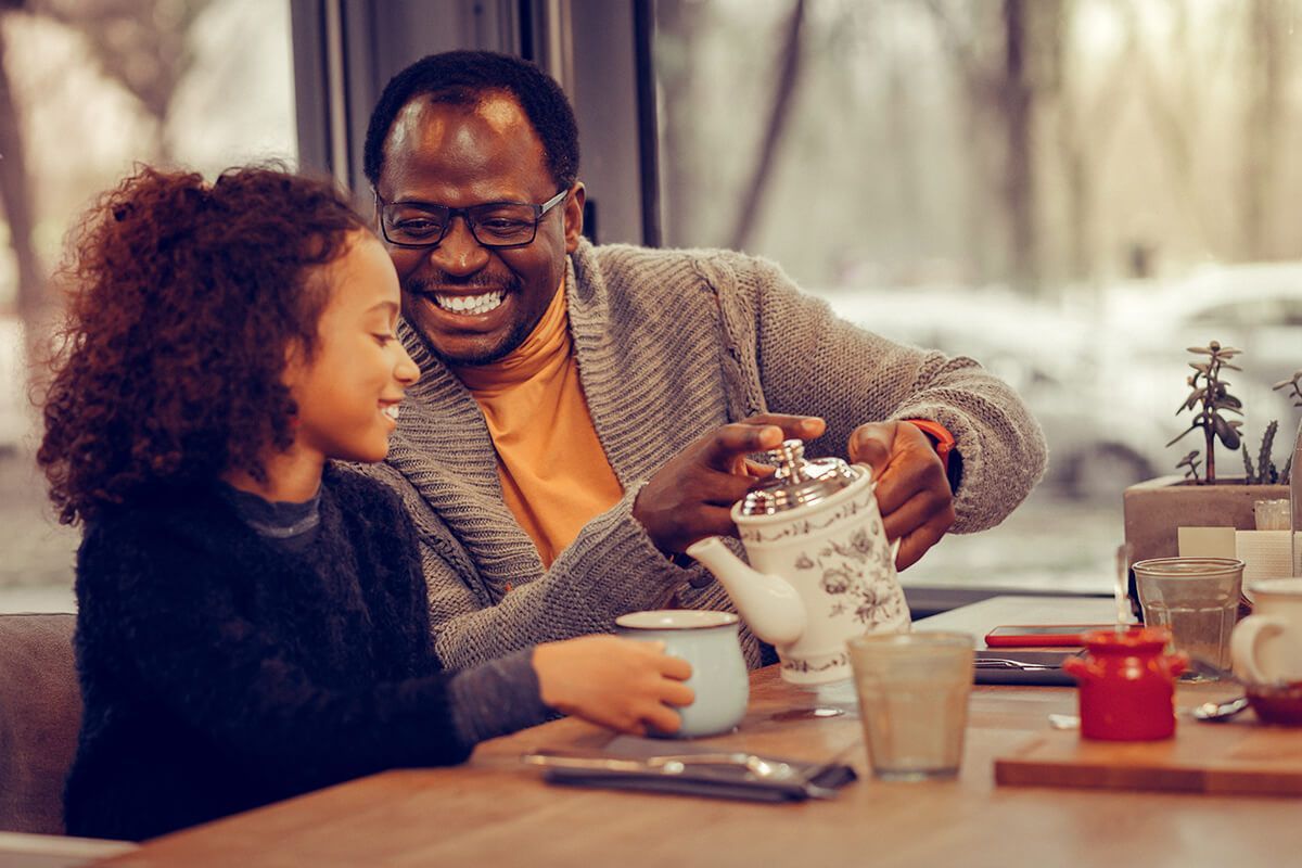 Um homem e uma menina estão sentados à mesa tomando chá.