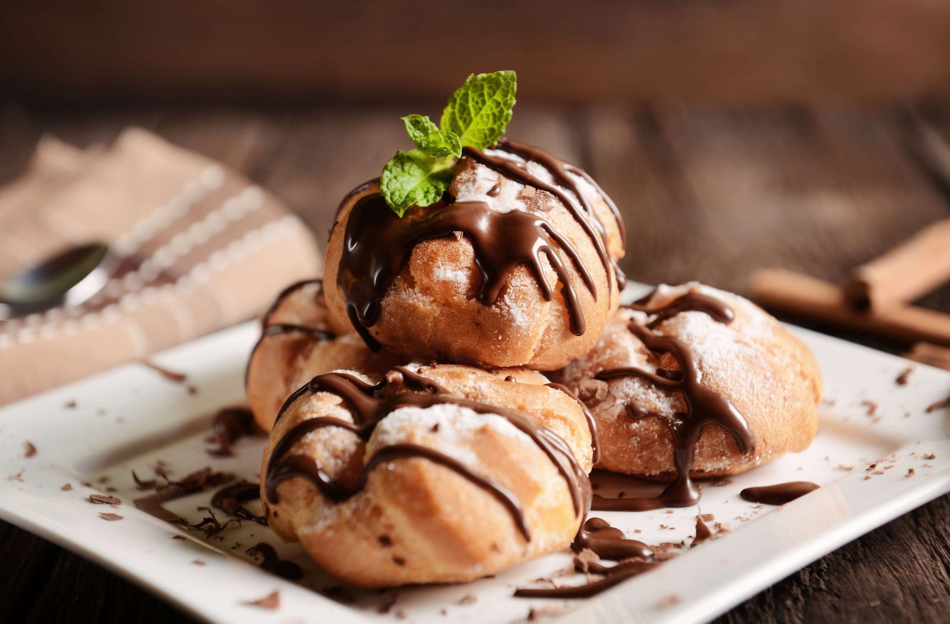 Um prato branco coberto com uma pilha de sobremesas com calda de chocolate e açúcar de confeiteiro.