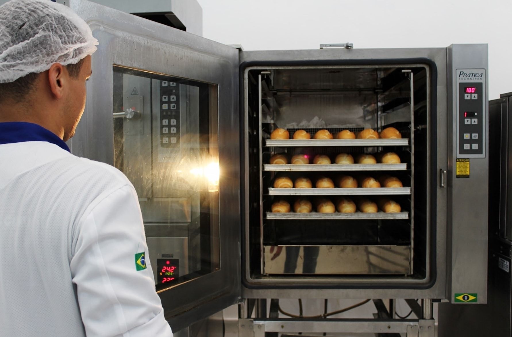 Um homem de jaleco branco está olhando para um forno cheio de pães