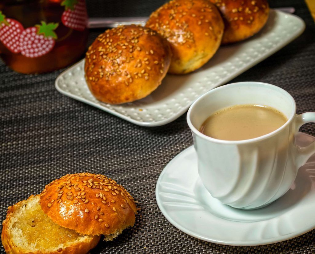 Uma xícara de café e um pãozinho em um pires sobre uma mesa.