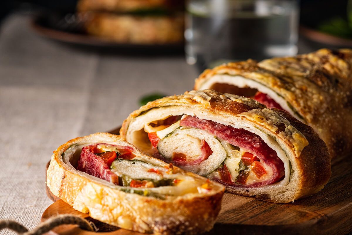 Um pedaço de pão com carne e vegetais está sobre uma tábua de corte de madeira.