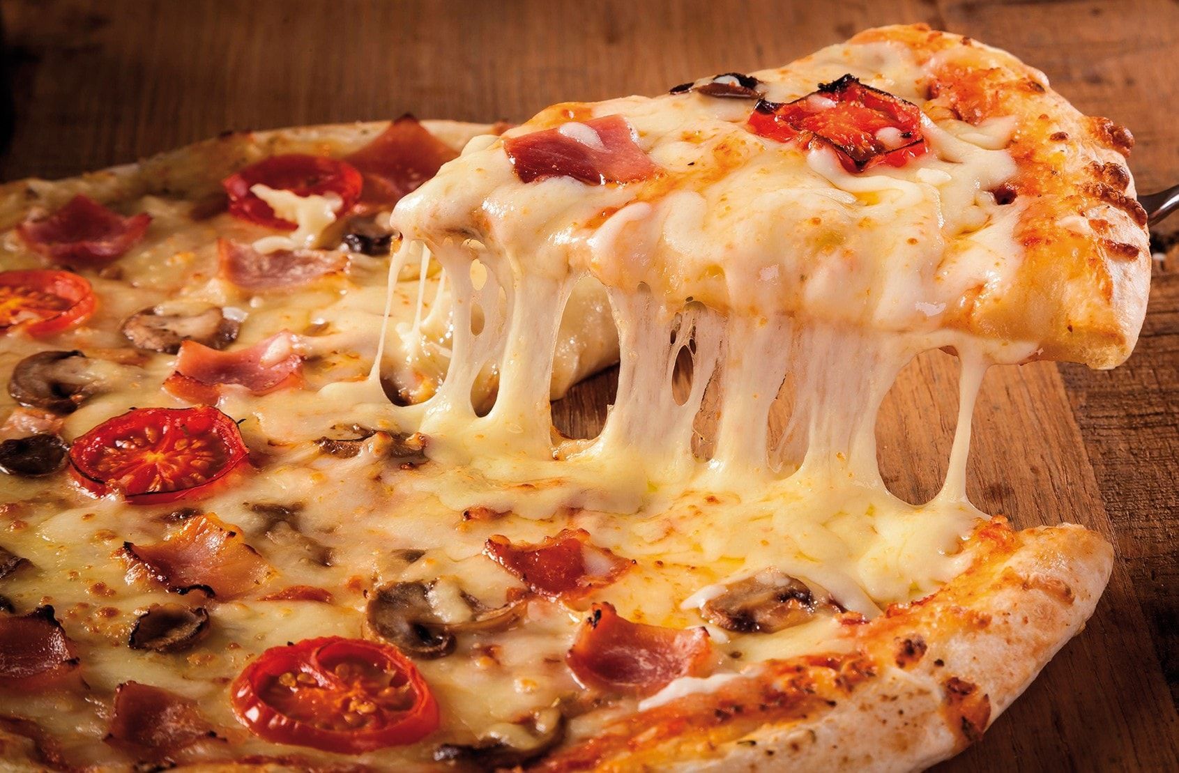 Uma pizza com uma fatia retirada dela sobre uma mesa de madeira.