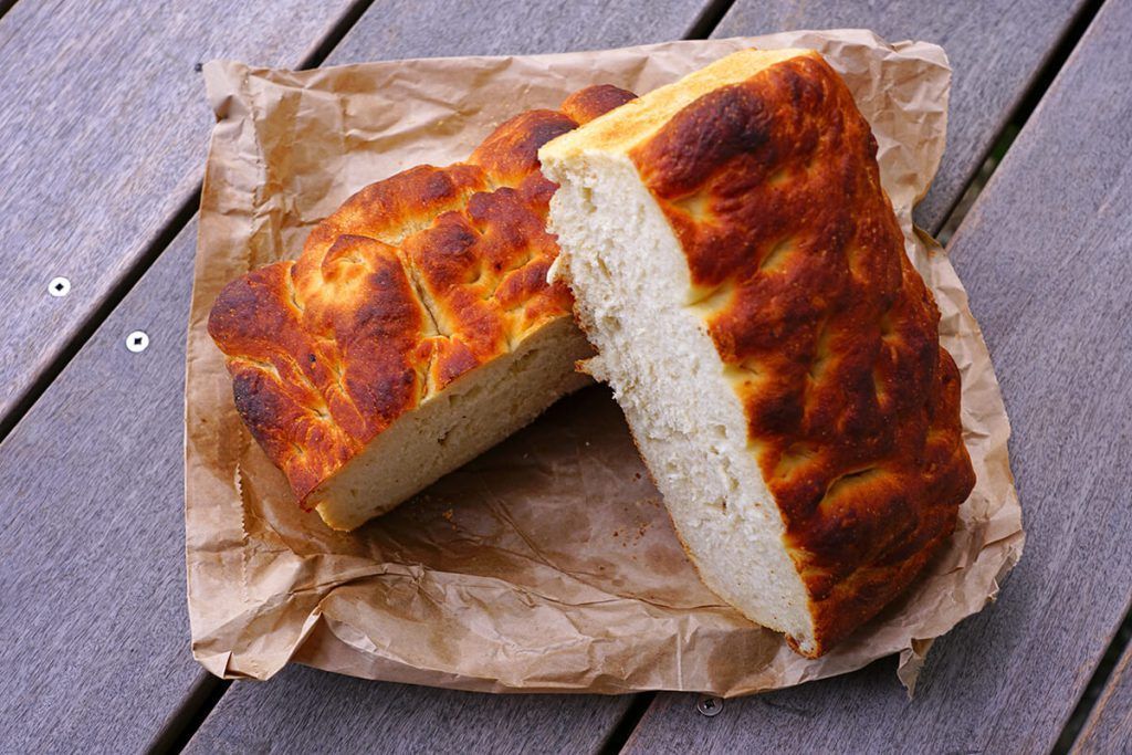 Duas fatias de pão estão sobre um pedaço de papel pardo em uma mesa de madeira.
