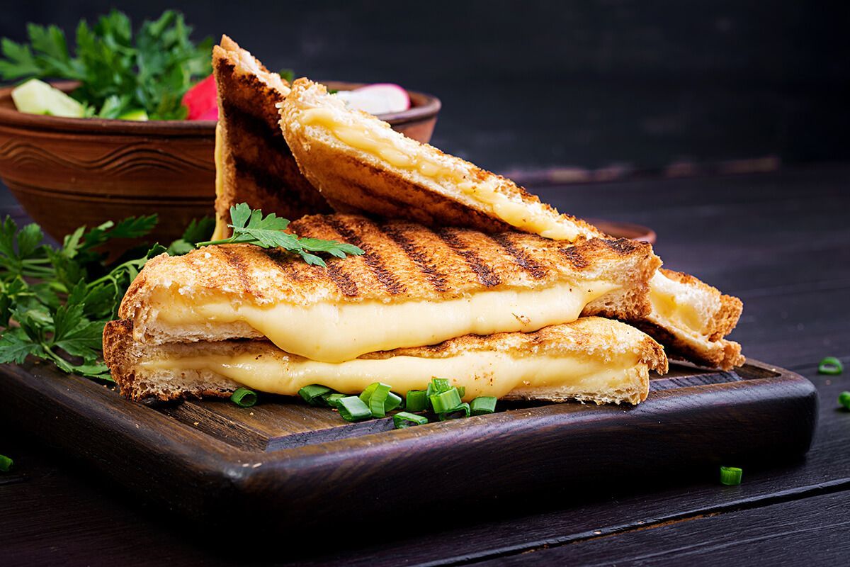 Um sanduíche de queijo grelhado está sobre uma tábua de corte de madeira.