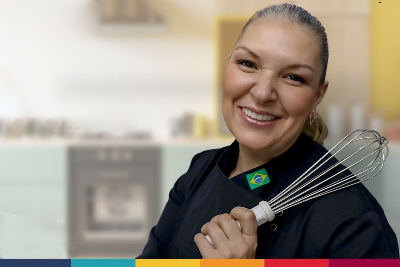 Uma mulher em uniforme de chef sorri enquanto segura um batedor
