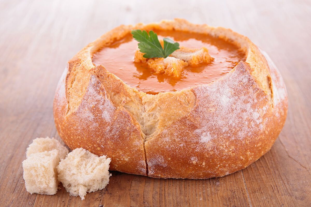 Uma tigela de sopa dentro de um pão sobre uma mesa de madeira.