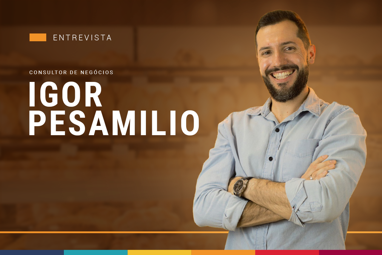 Um homem com barba está de pé com os braços cruzados e sorrindo.
