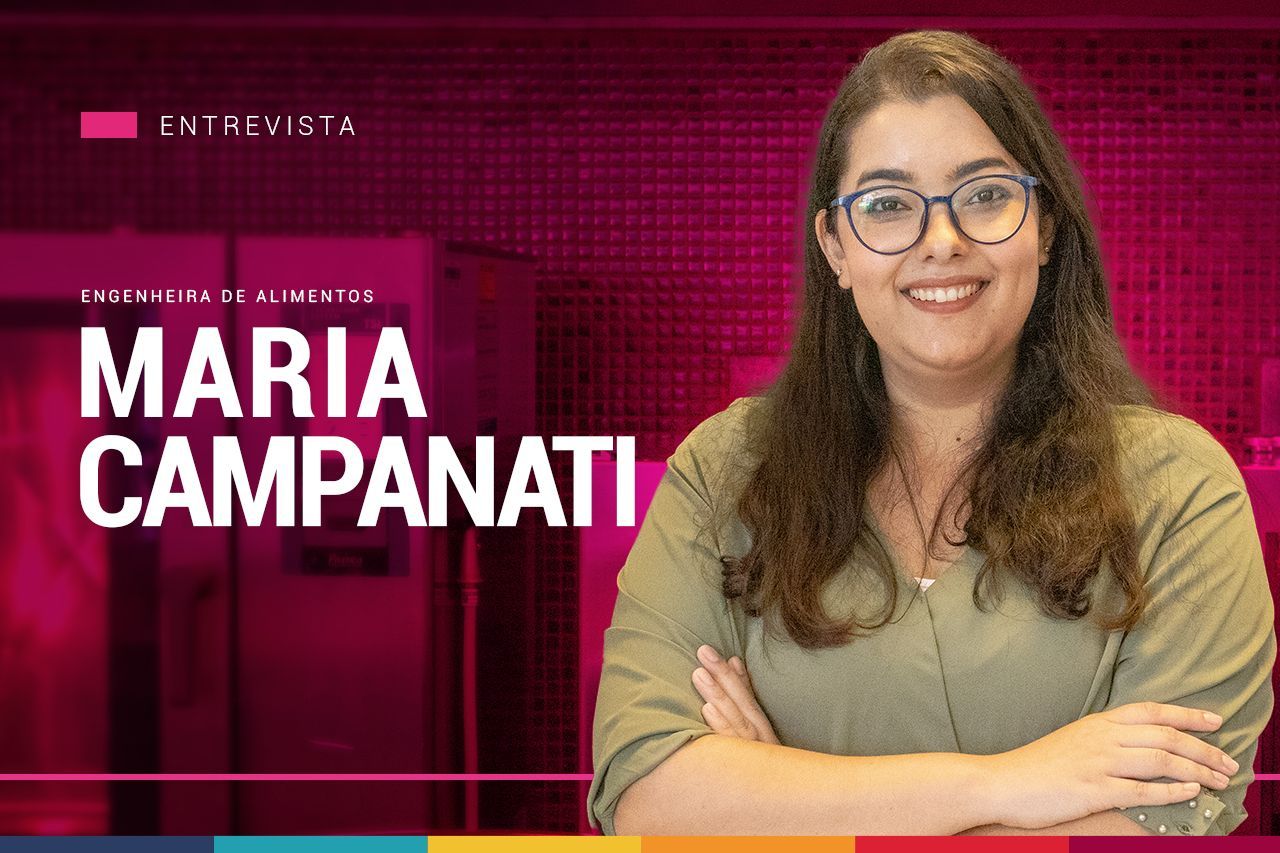 Uma mulher usando óculos e uma camisa verde está sorrindo com os braços cruzados.
