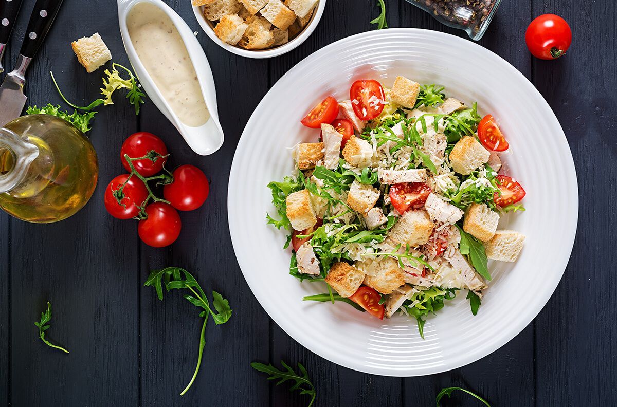 Uma salada com croutons, tomates e alface em uma tigela branca sobre uma mesa.