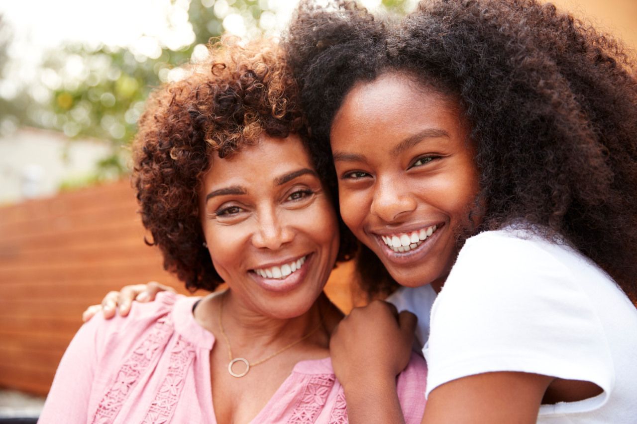 Uma mãe e filha estão posando para uma foto juntas e sorrindo.