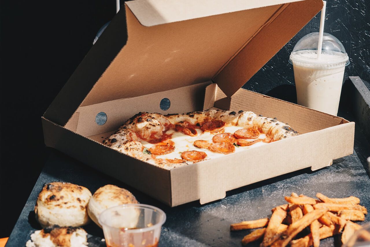 Uma caixa de pizza cheia de pizza e batatas fritas sobre uma mesa.