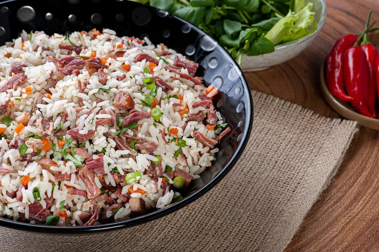 Uma tigela de arroz com carne e vegetais em uma mesa de madeira.