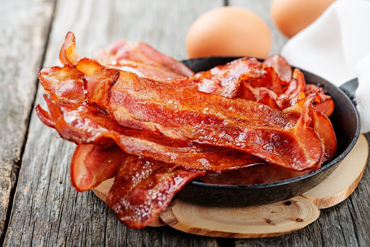 Uma panela cheia de bacon e ovos sobre uma mesa de madeira.