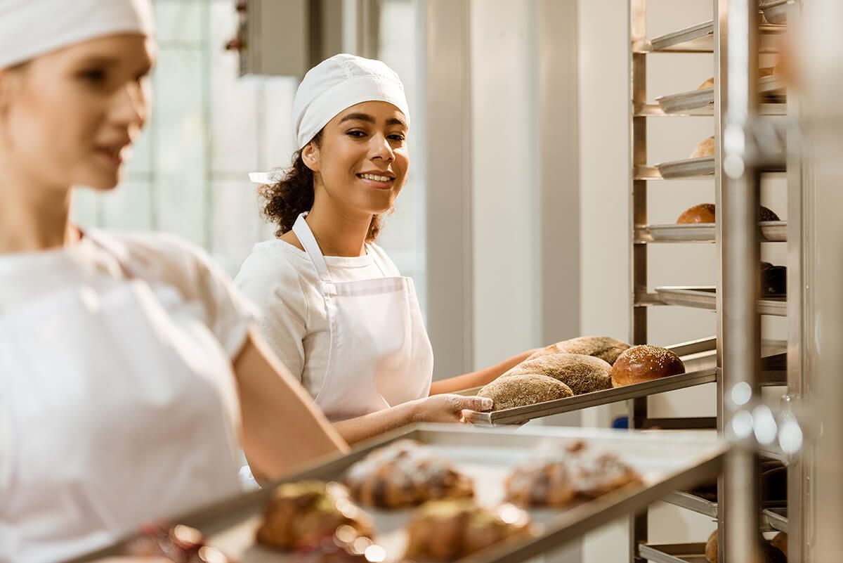 Uma mulher está segurando uma bandeja de croissants em uma padaria.