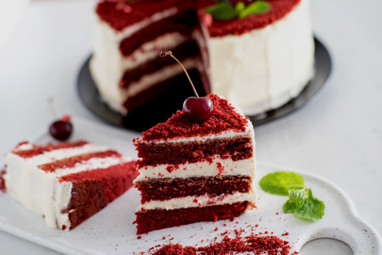 Uma fatia de bolo red velvet com uma cereja no topo em um prato.
