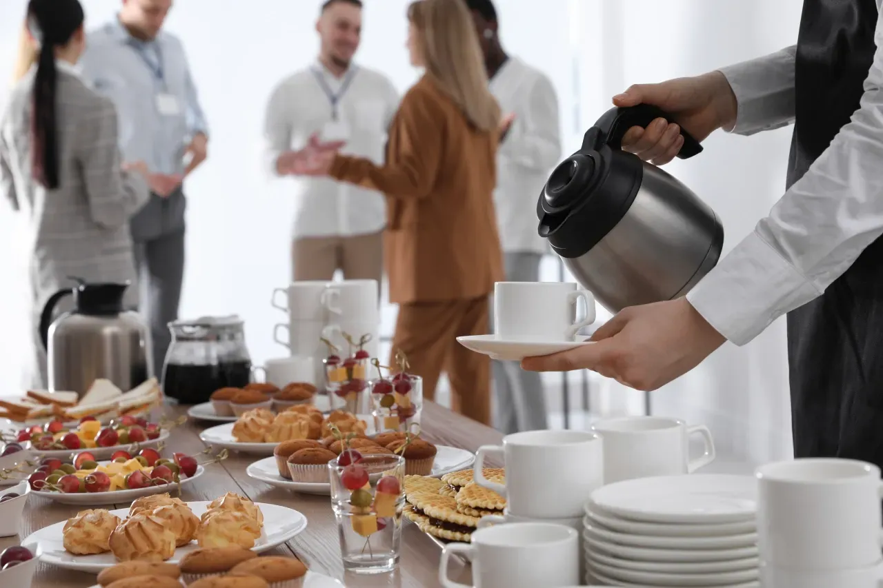 Um garçom está servindo café em xícaras em uma mesa de bufê.