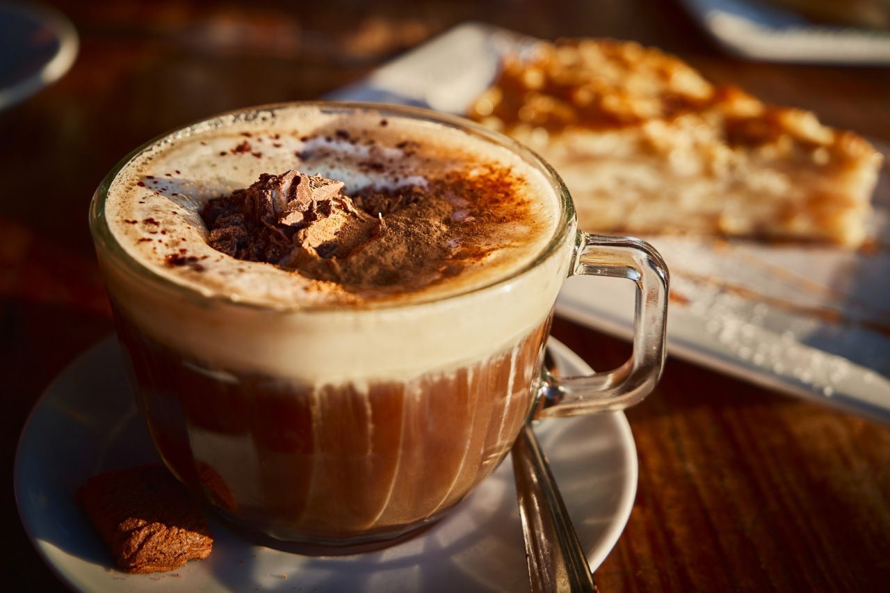 Uma xícara de café em um pires ao lado de um pedaço de bolo.