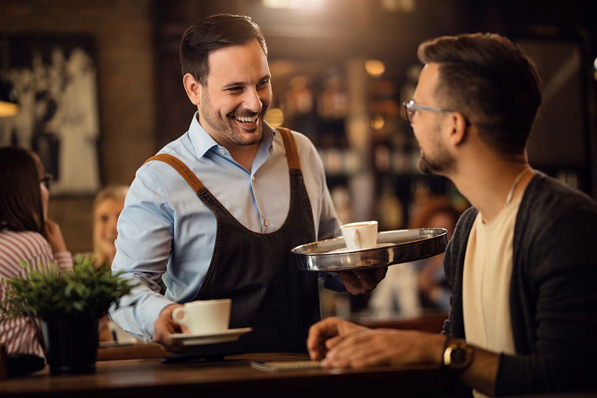 Um garçom está servindo uma xícara de café para um homem em um restaurante.
