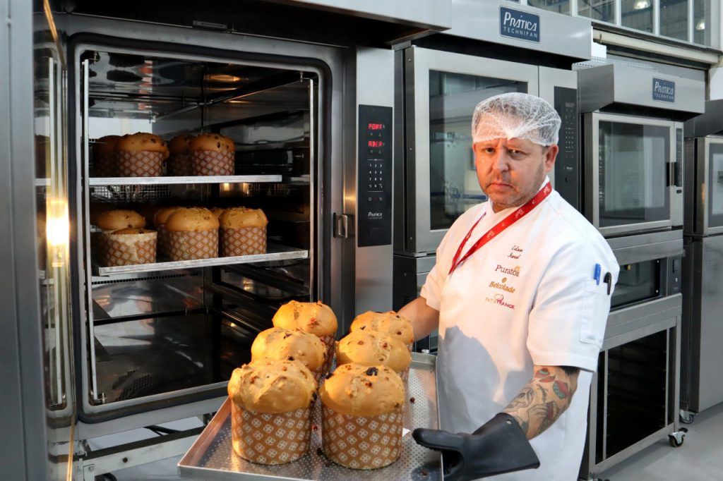 Um homem está segurando uma bandeja de cupcakes em frente ao forno.