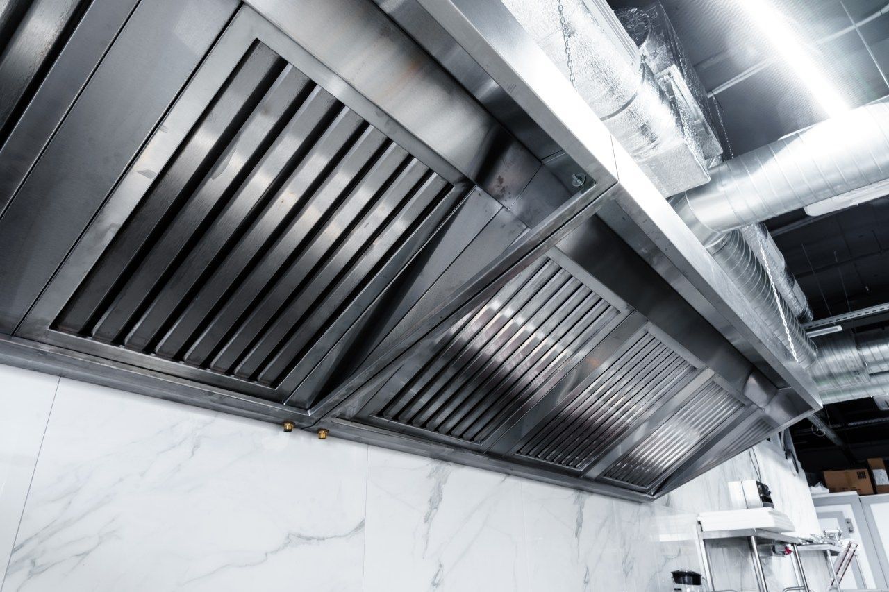Um exaustor de aço inoxidável está pendurado no teto de uma cozinha.