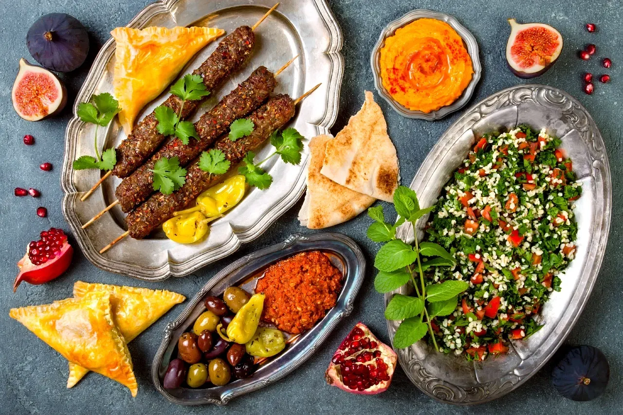 Prato com alimentos halal, incluindo espetos de carne, tabule, pão árabe, homus, azeitonas e acompanhamentos típicos da culinária do Oriente Médio.