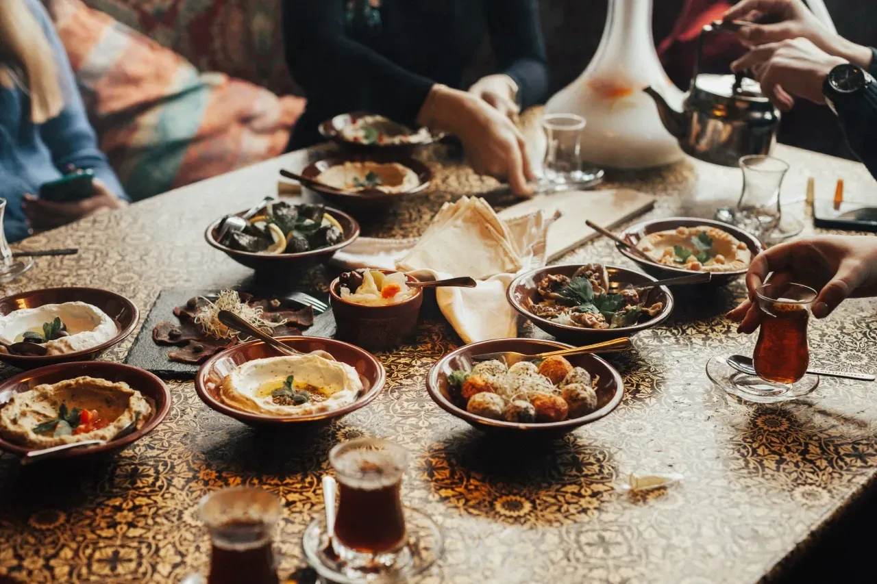 Comida libanesa servida em estilo mezze, com homus, falafel, pão sírio, folhas de uva e chá, em mesa