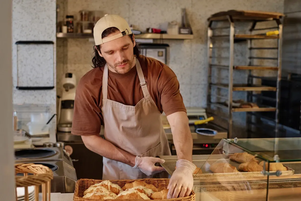 Um homem de avental está cortando pão em uma padaria.