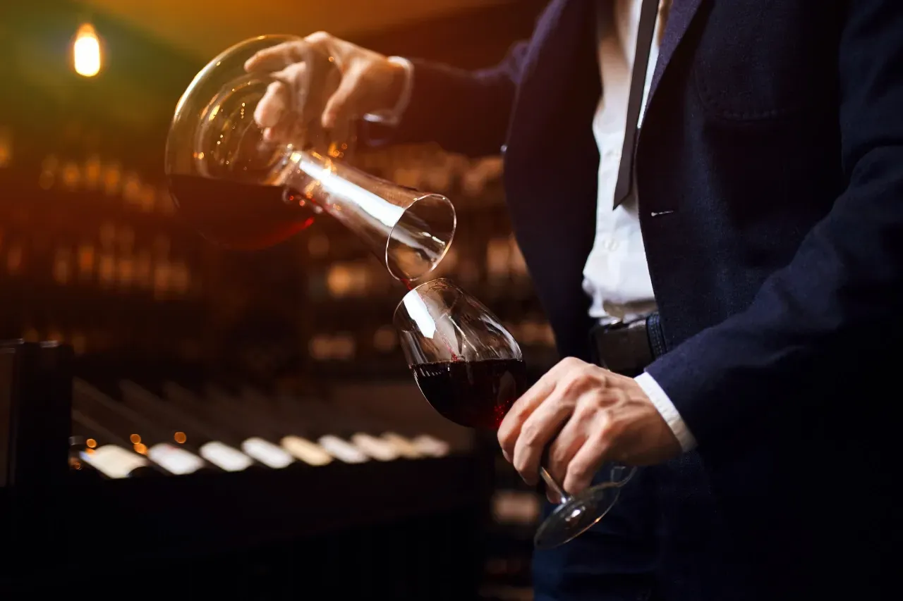 Homem servindo vinho tinto de um decanter para uma taça.