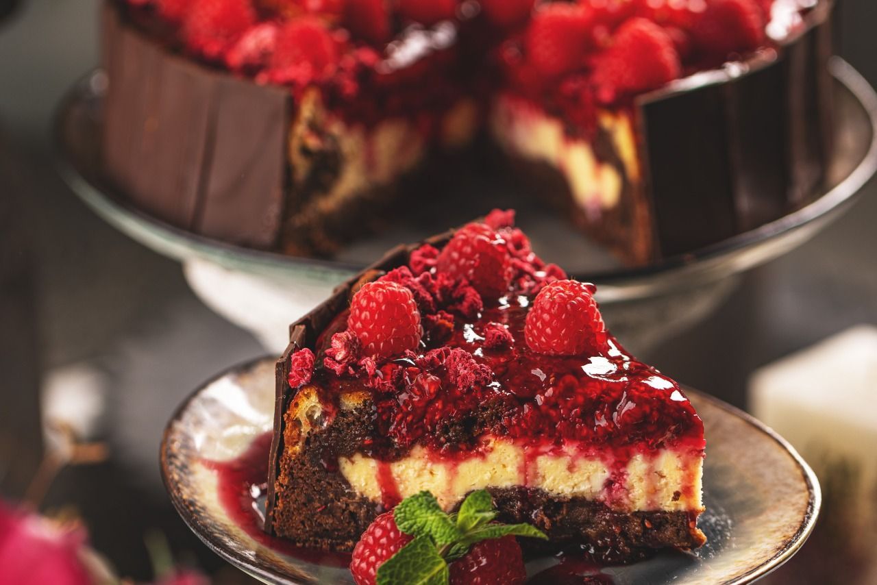 Uma fatia de cheesecake com framboesas por cima está em um prato.