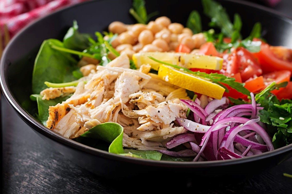 Uma salada com frango, grão-de-bico, espinafre, tomate e cebola em uma tigela preta.