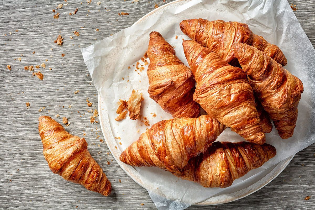 Um prato branco coberto com croissants sobre uma mesa de madeira.