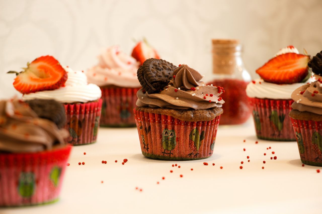 Um grupo de cupcakes com morangos e cobertura de chocolate sobre uma mesa.