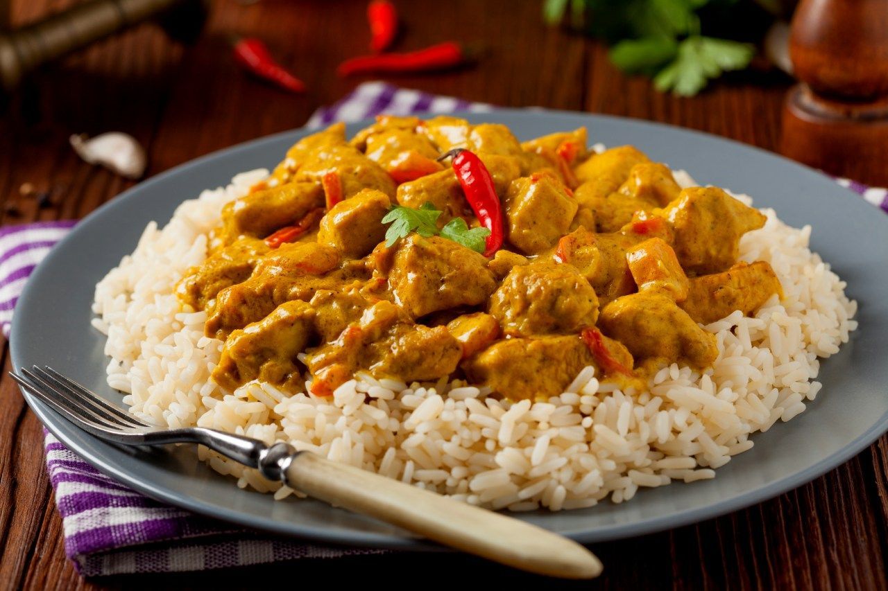 Um prato de curry de frango com arroz e um garfo sobre uma mesa de madeira.