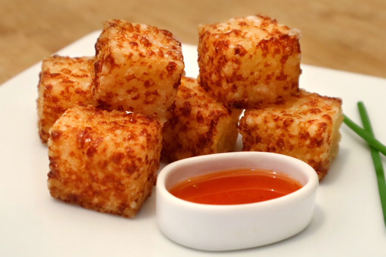 Um prato branco coberto com cubos de queijo e uma pequena tigela de molho