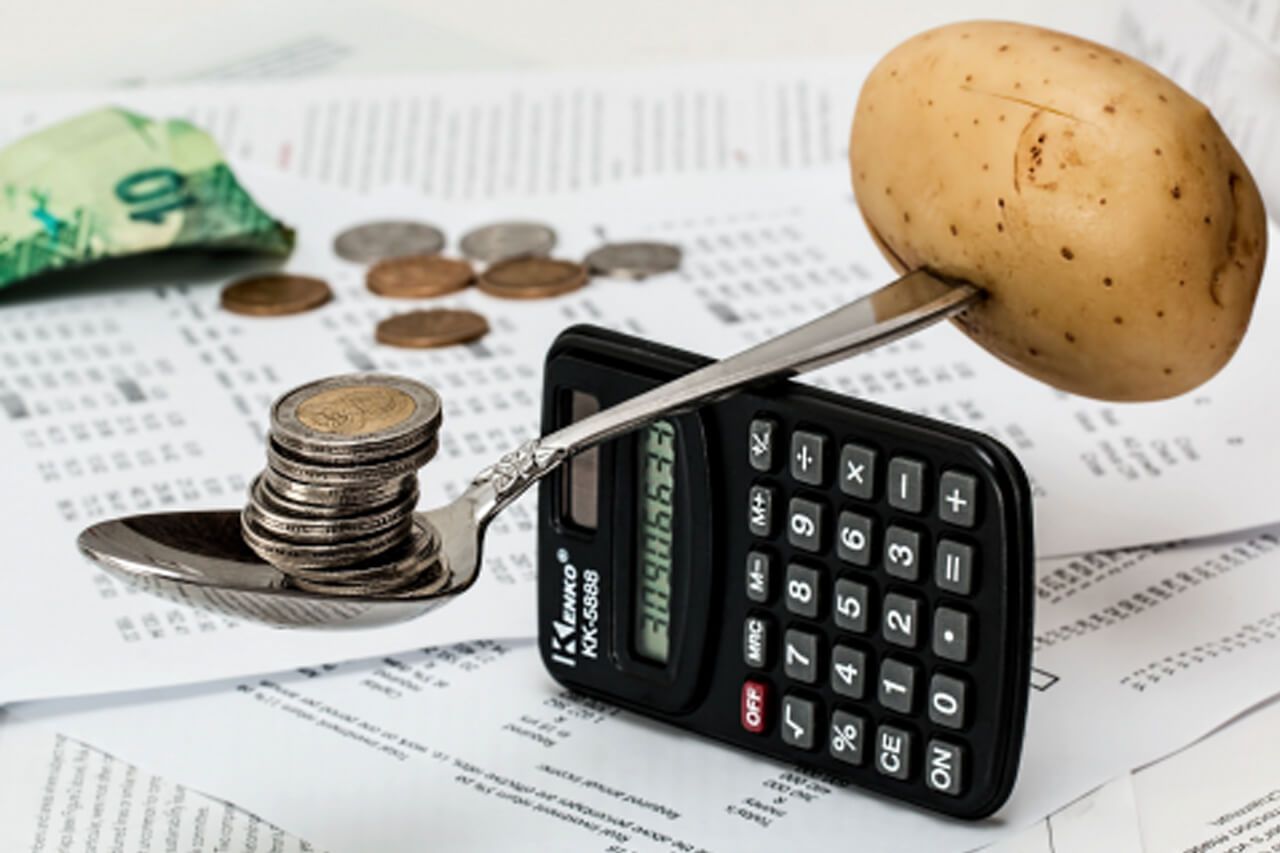 Uma batata está em cima de uma calculadora ao lado de uma pilha de moedas.