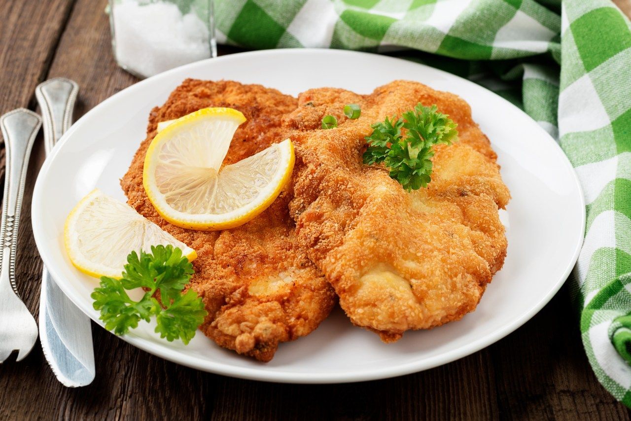 Um prato de frango frito com rodelas de limão e salsa sobre uma mesa de madeira.
